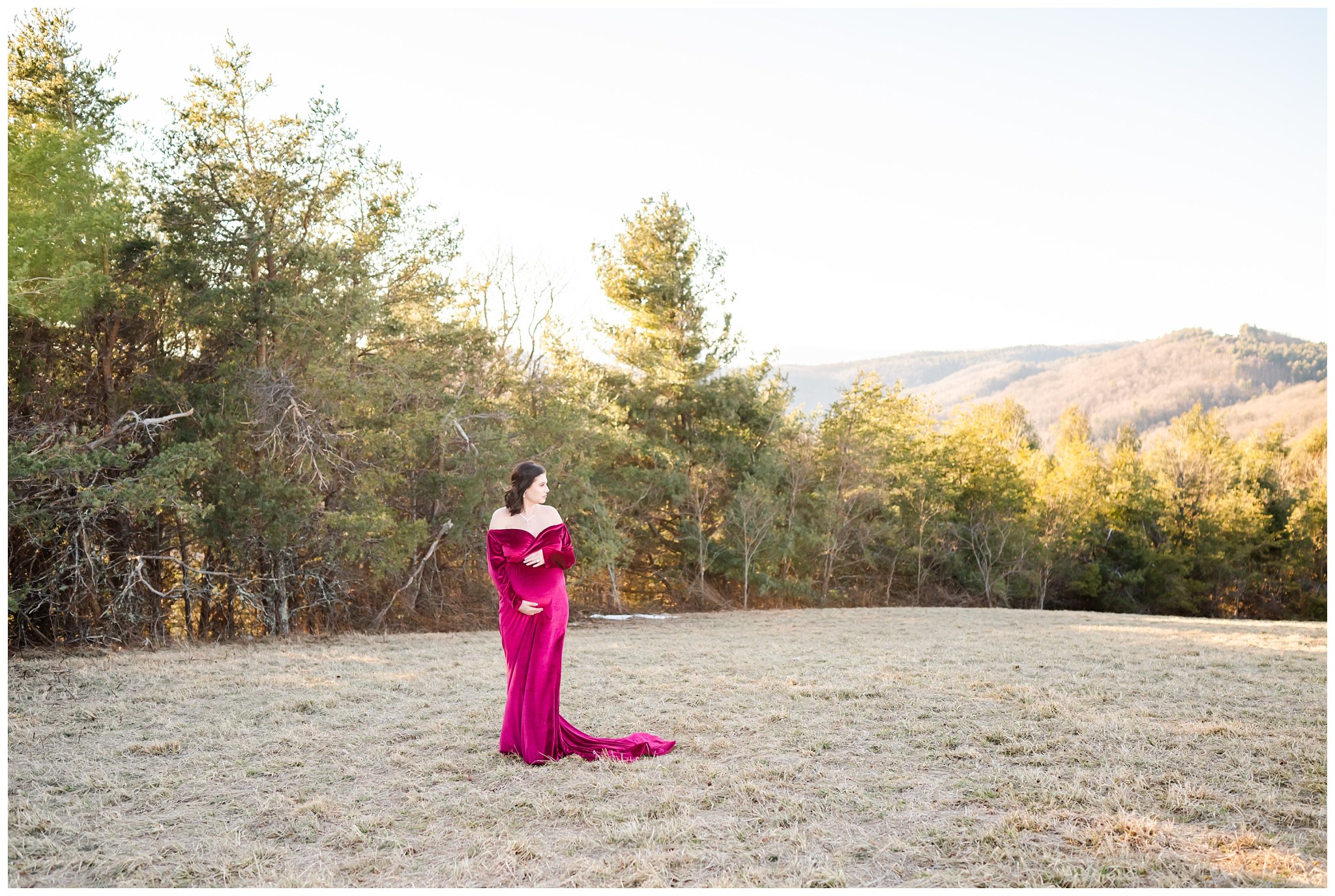 expectant mother poses in magenta dress for maternity session with rolling hills behind her