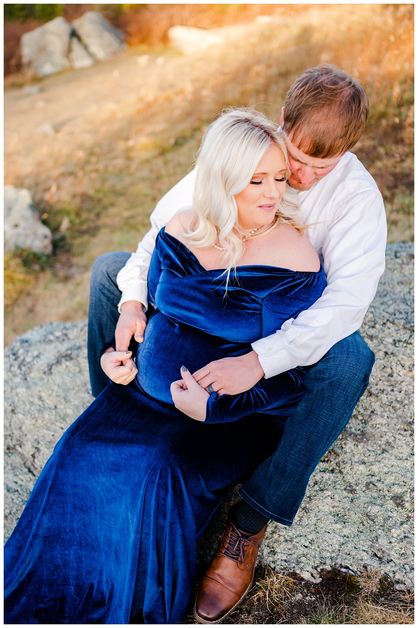 couple sitting on rock for maternity session mom in blue velvet dress