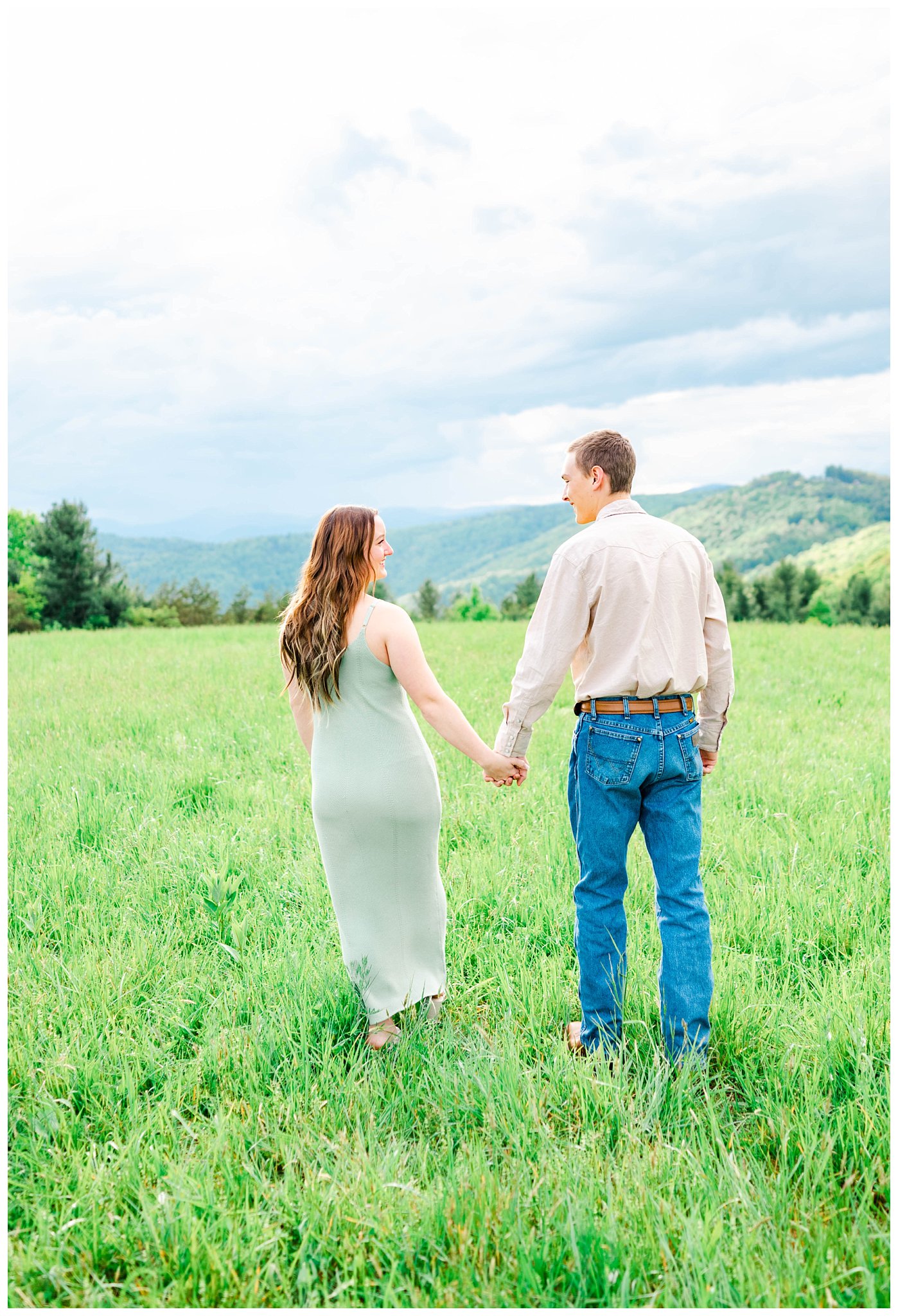 couple holding hands and walking in grass for their mountain top engagement session