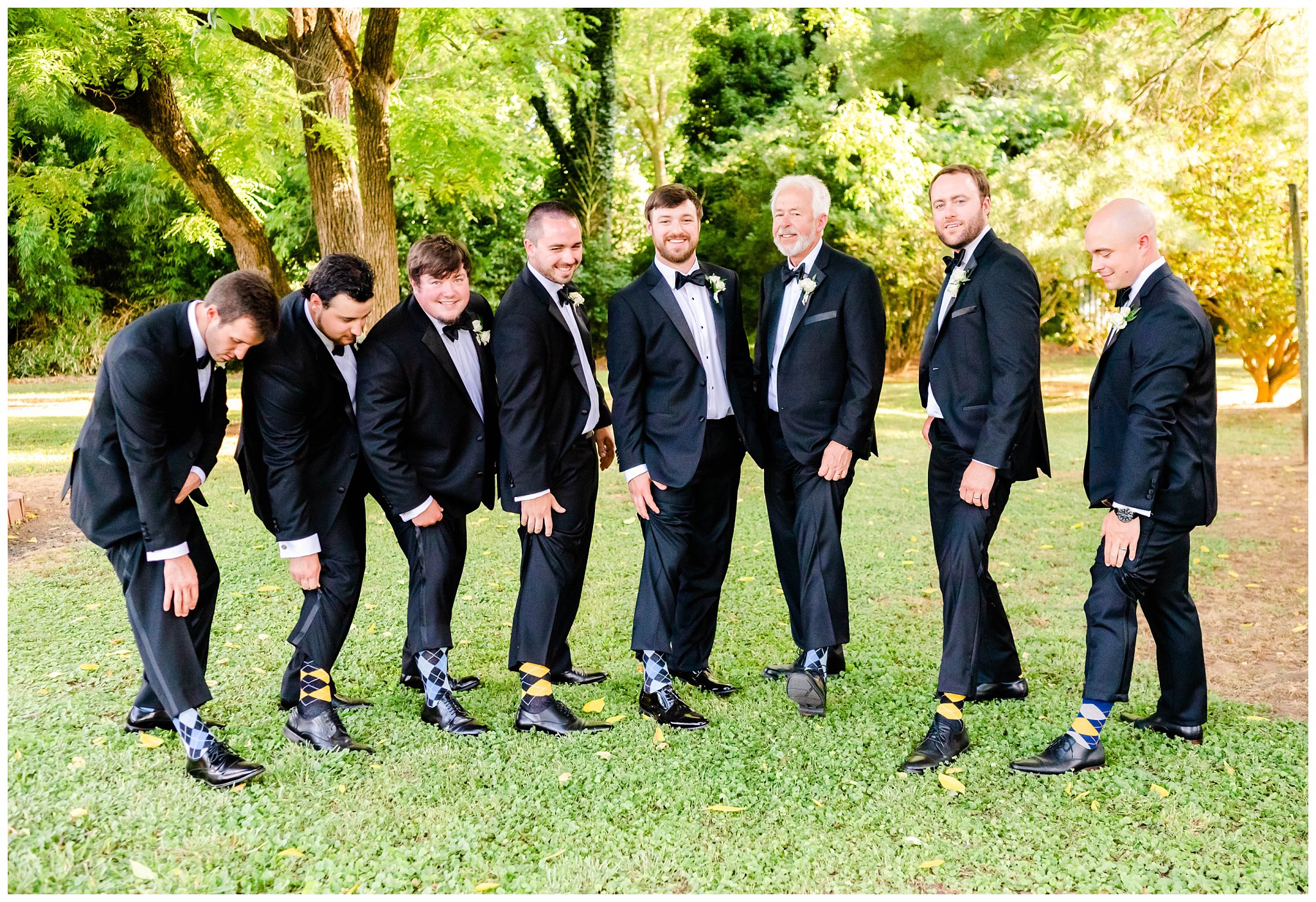 groom and groomsmen pose by showing off their socks outdoors